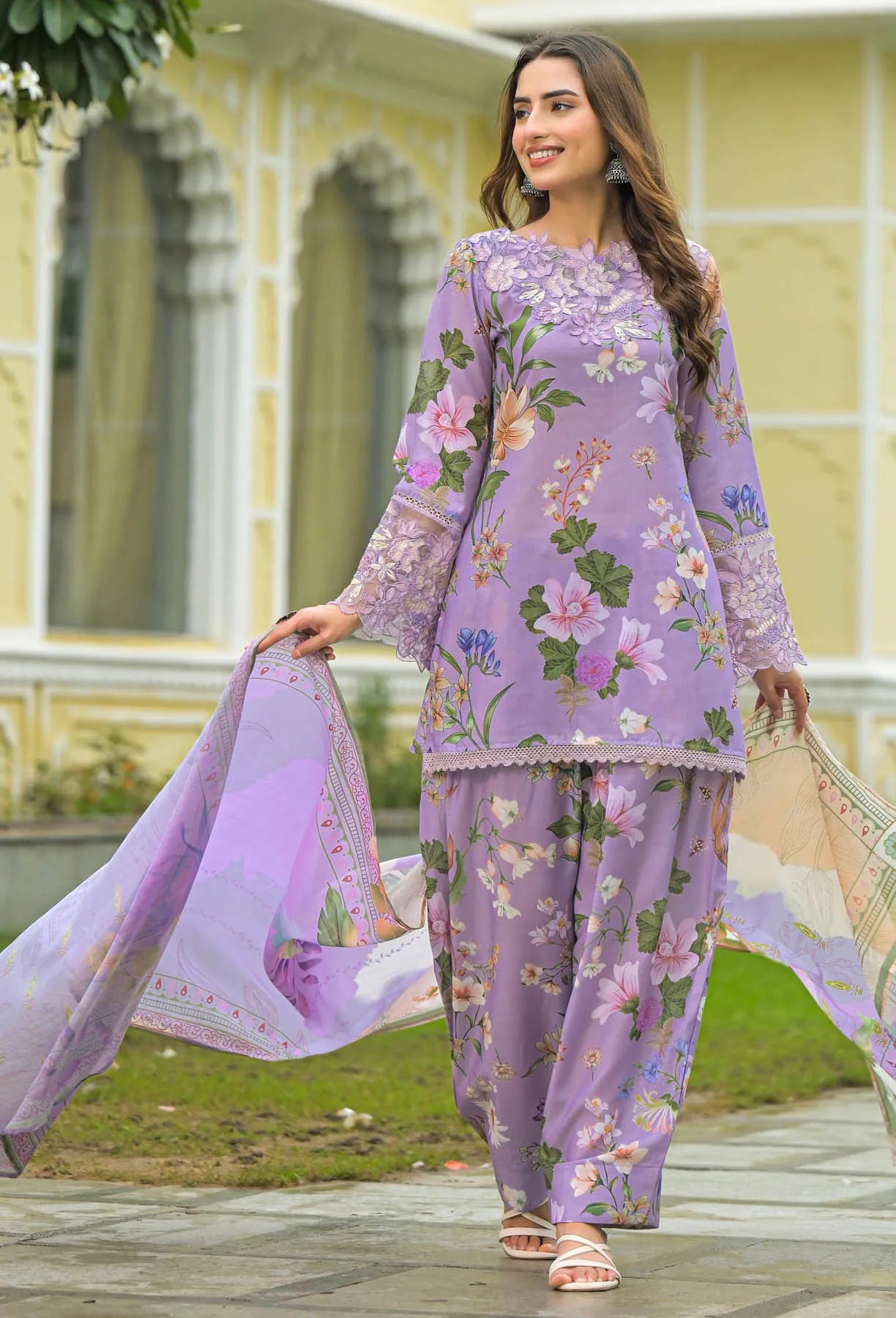 Woman in a floral purple outfit standing outdoors with a building in the background