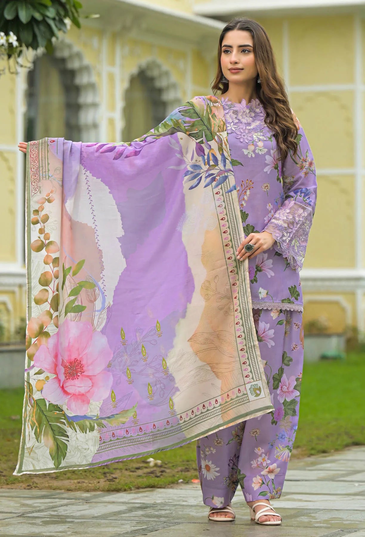 Woman in a floral outfit holding a matching scarf outdoors.