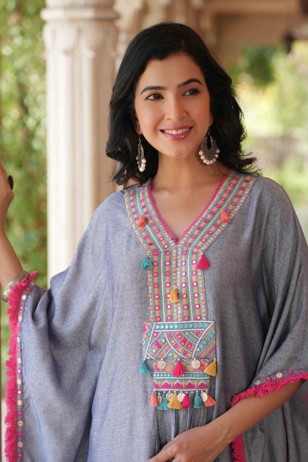 Woman wearing a gray traditional outfit with colorful embroidery and tassels.