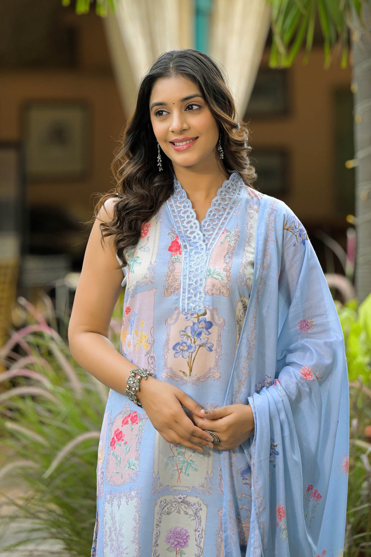 Woman wearing a light blue embroidered traditional outfit with floral patterns, standing outdoors.