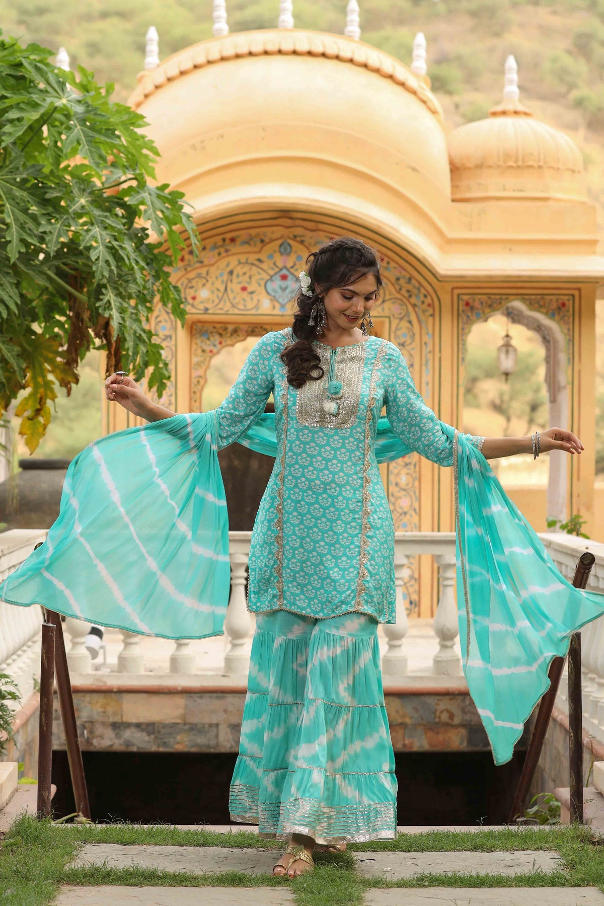 Woman in a turquoise traditional outfit standing in front of a decorative building with domes.