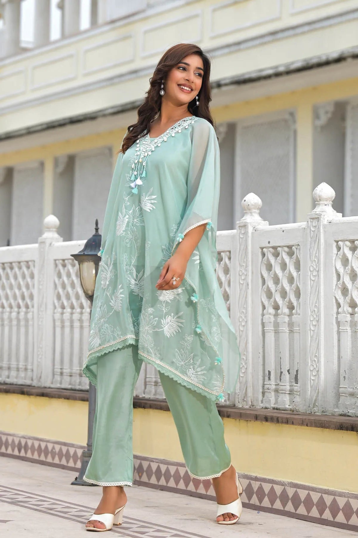 Woman wearing a light green traditional outfit with white embroidery in front of a white building.