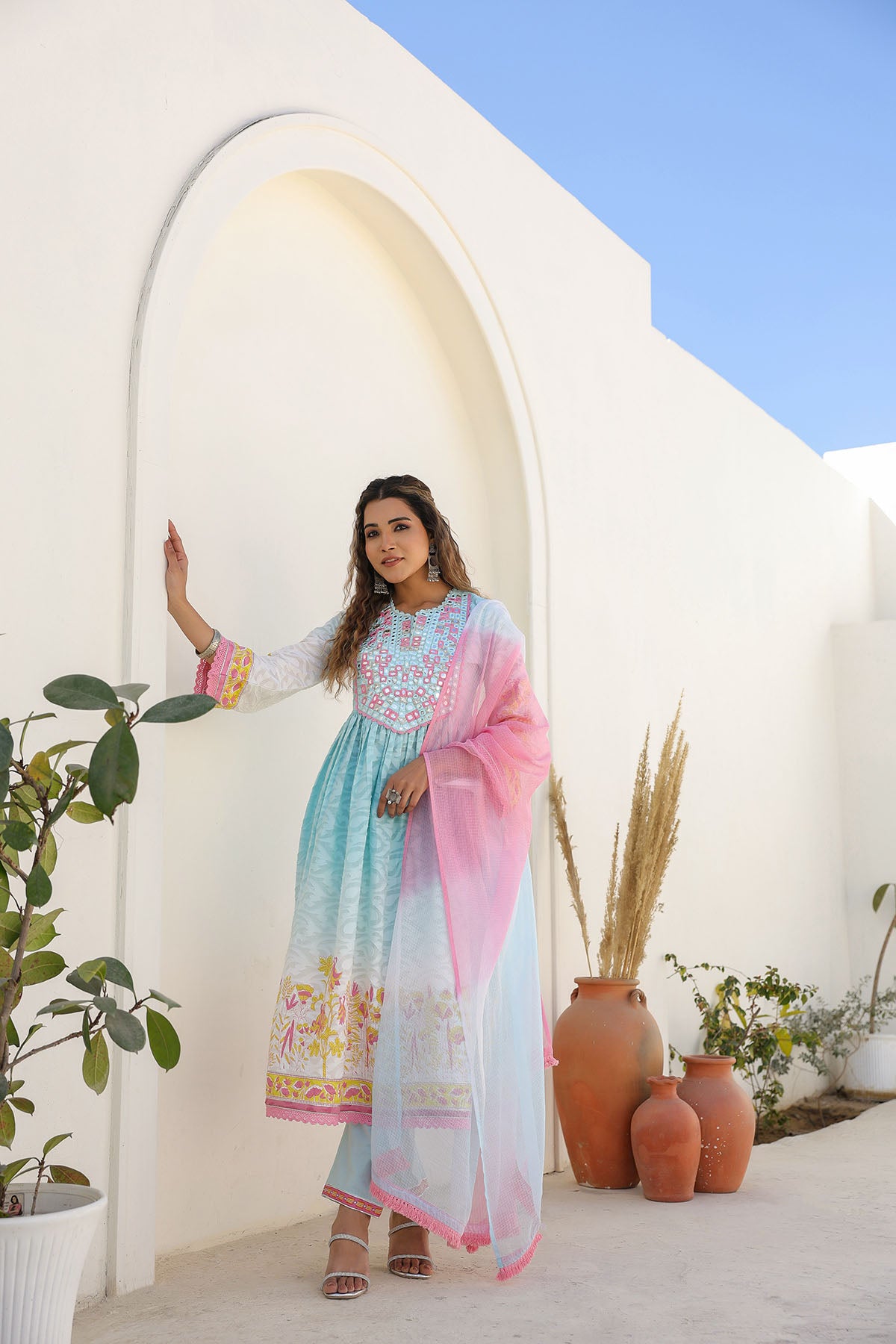 Woman in a colorful dress standing in front of a white archway with plants and vases.