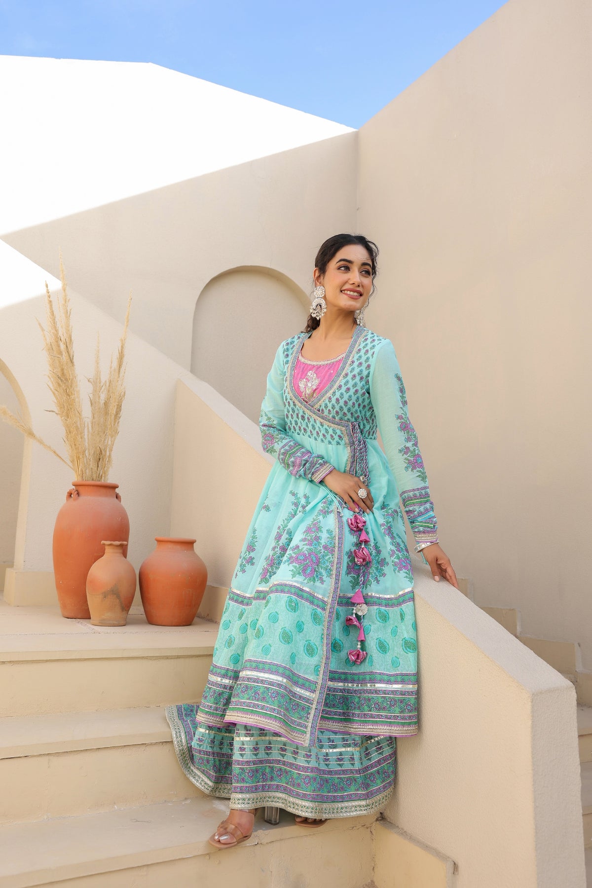 Woman in a teal traditional outfit standing on steps with a blue sky background