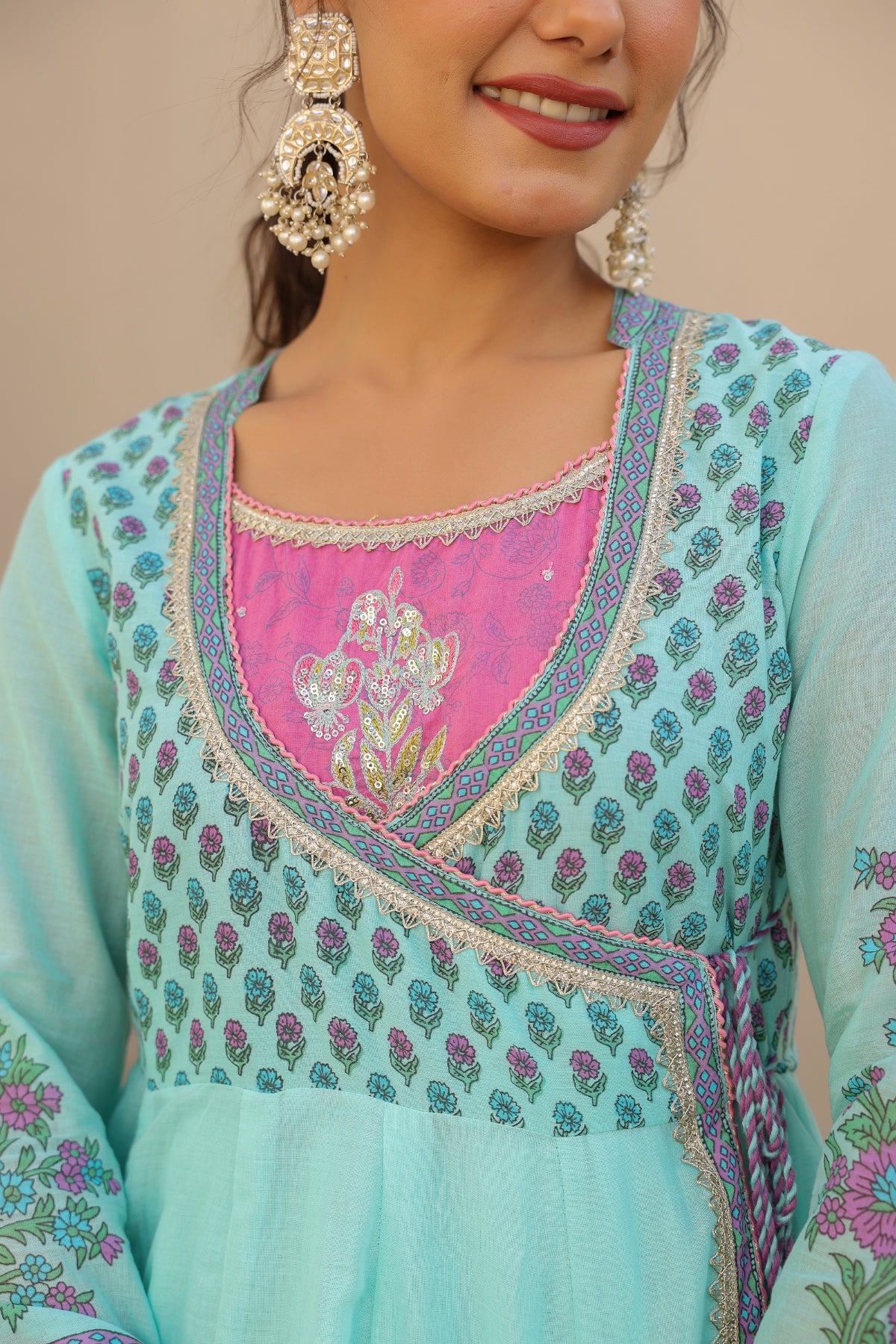 Woman wearing a light blue embroidered dress with pink inner lining against a beige background