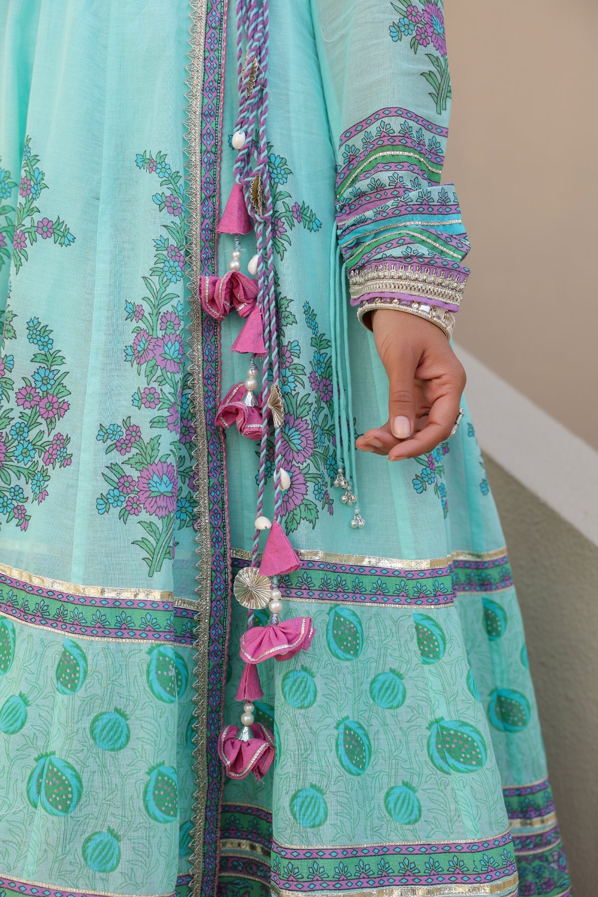 Turquoise traditional outfit with floral patterns and pink decorative elements on a neutral background