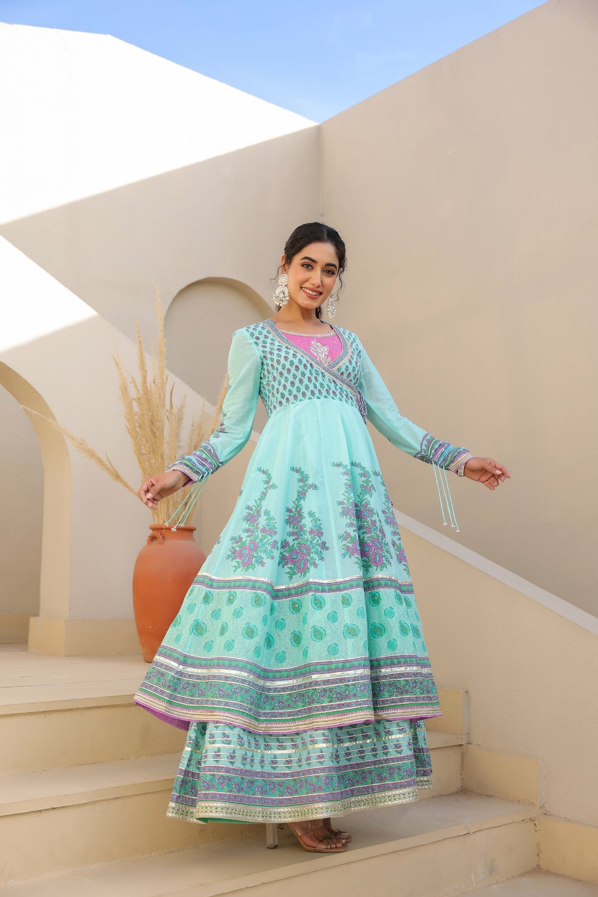 Woman in a light blue embroidered dress standing on steps with a decorative background