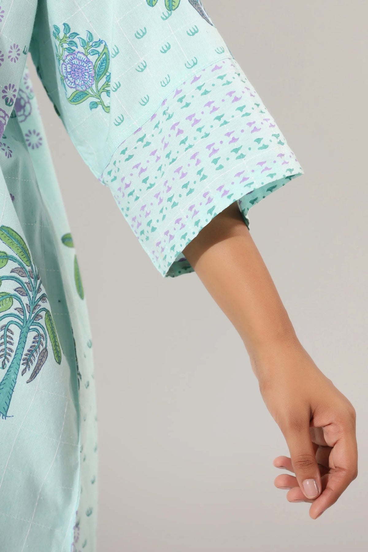 Light green fabric with floral patterns and a hand holding it against a neutral background