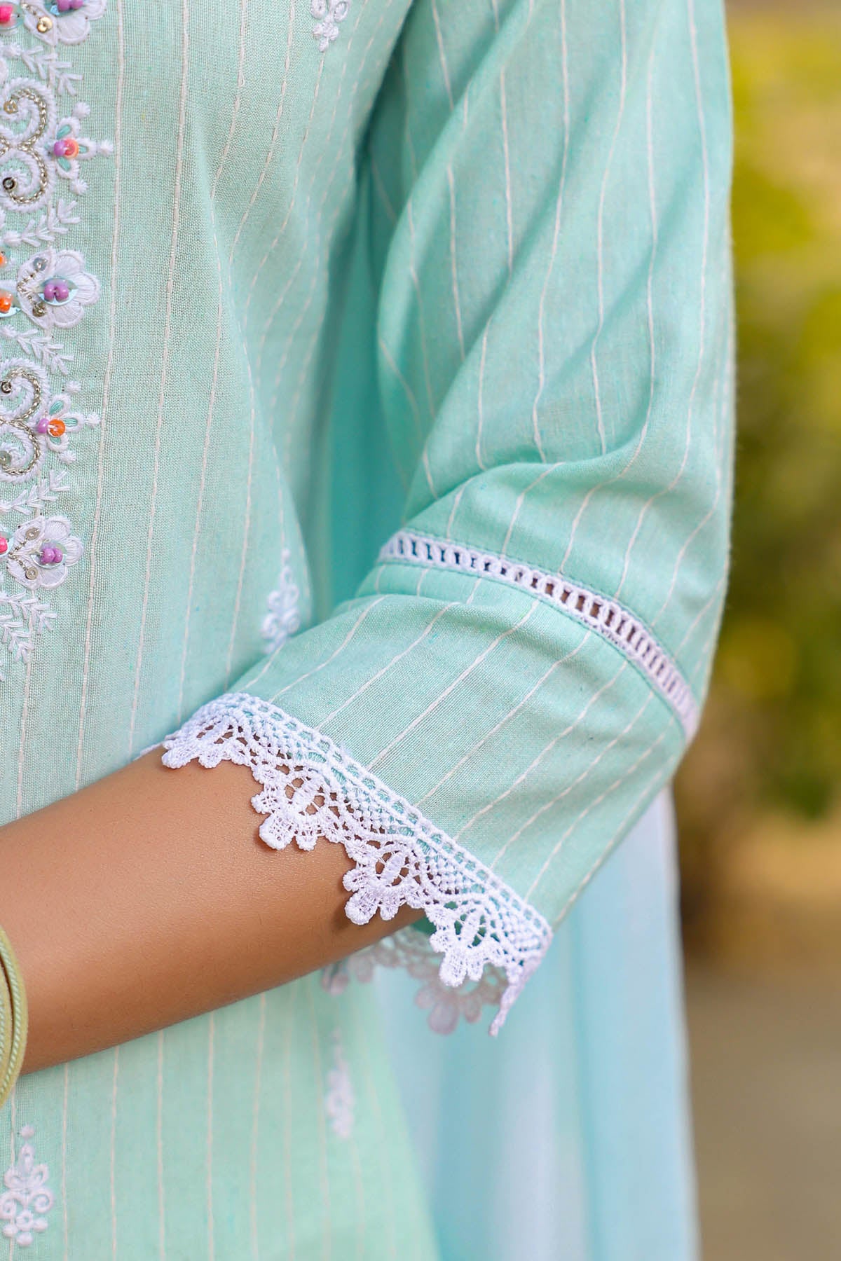 Light blue traditional outfit with lace detailing on a blurred natural background
