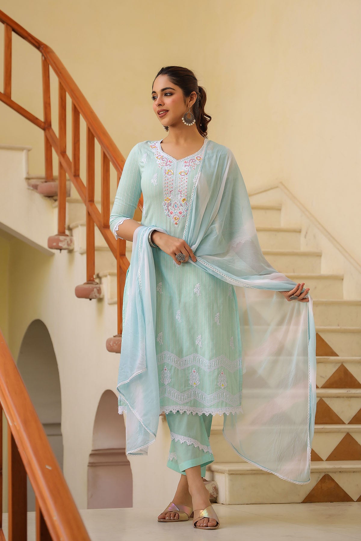 Woman in a light blue traditional outfit standing on a staircase.