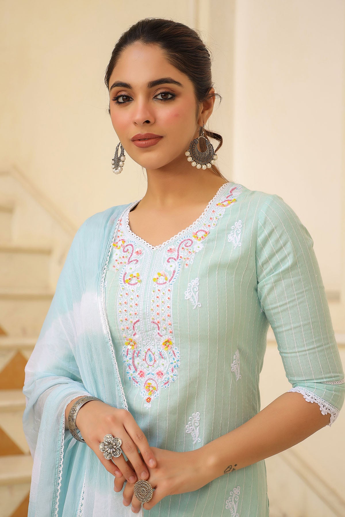 Woman wearing a light blue embroidered traditional outfit with a neutral background