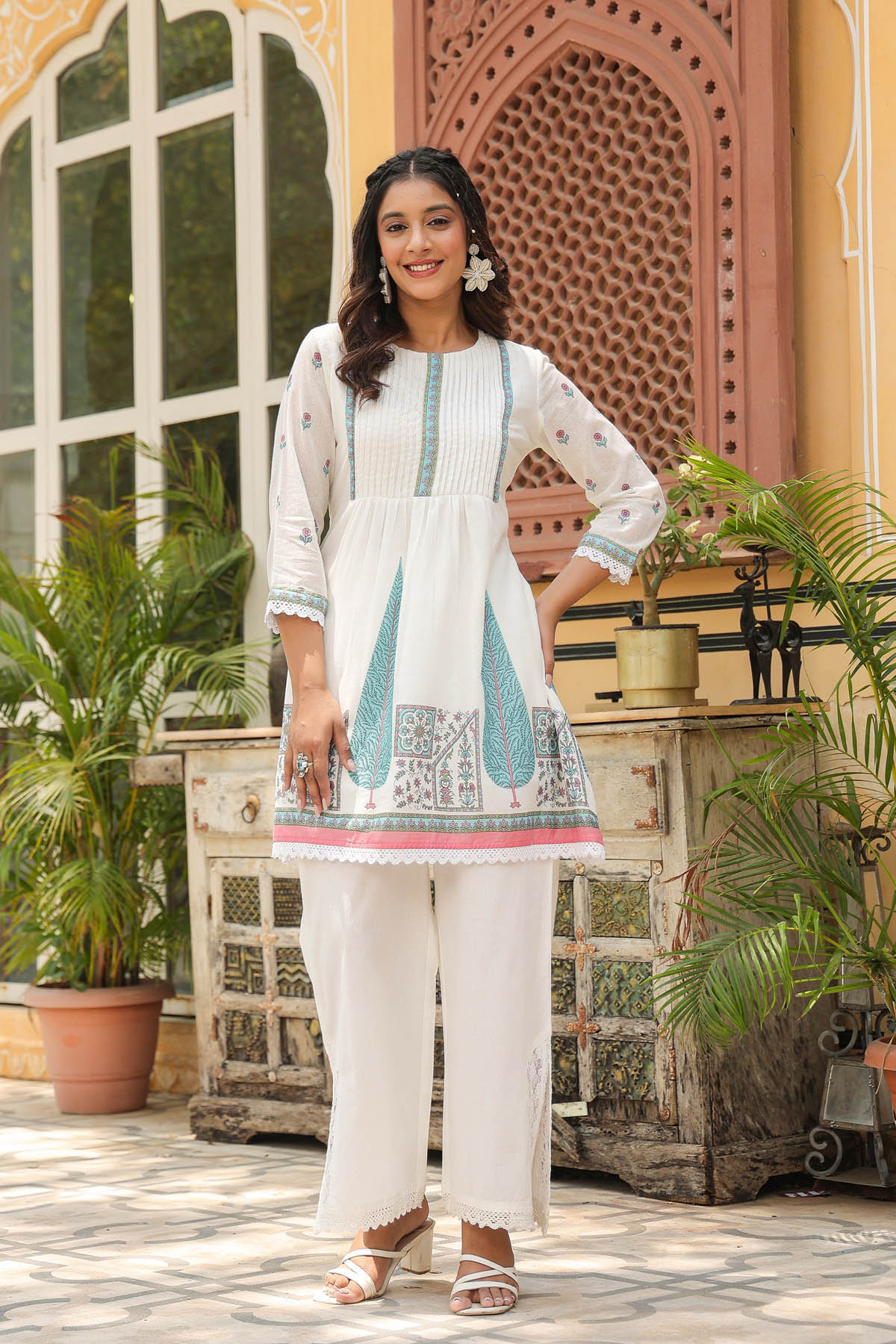 Woman in a white traditional outfit with blue patterns standing in front of a decorative building.
