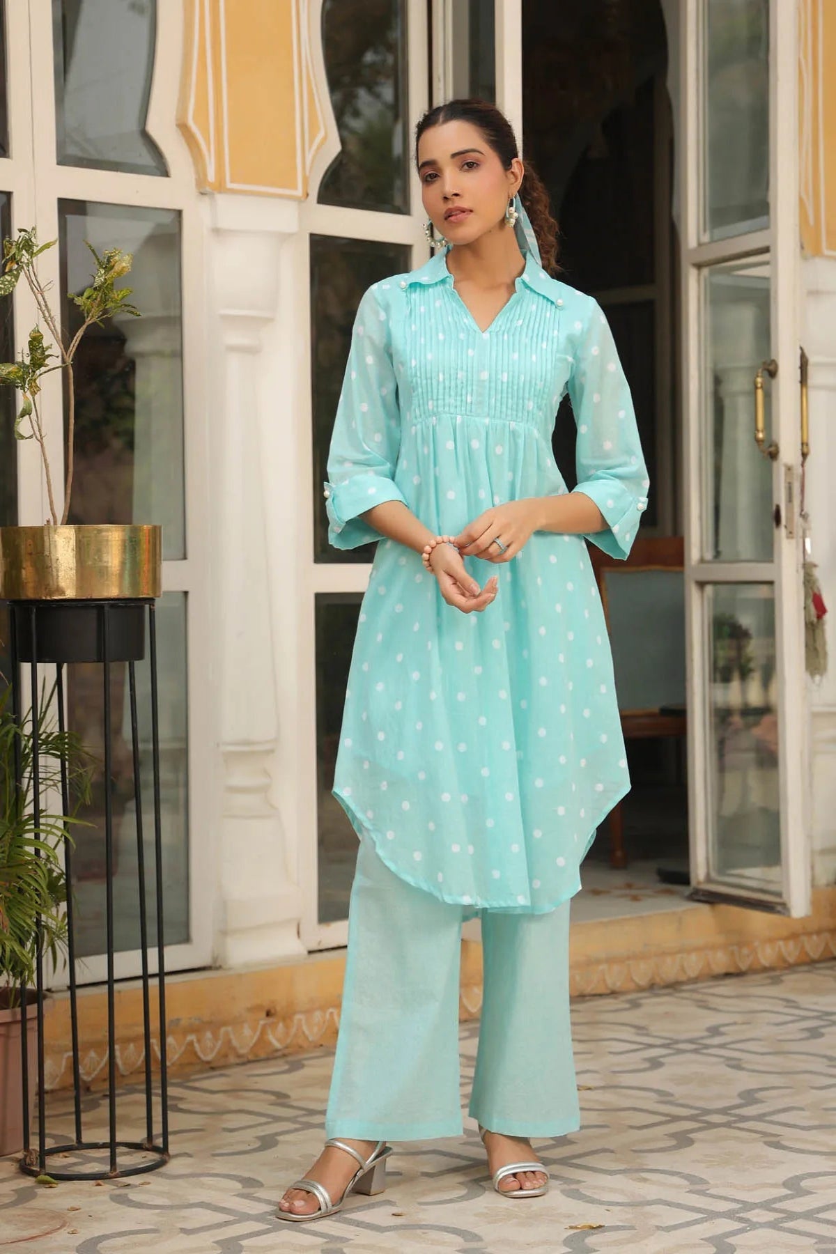 Woman wearing a light blue traditional outfit standing in front of a building entrance.