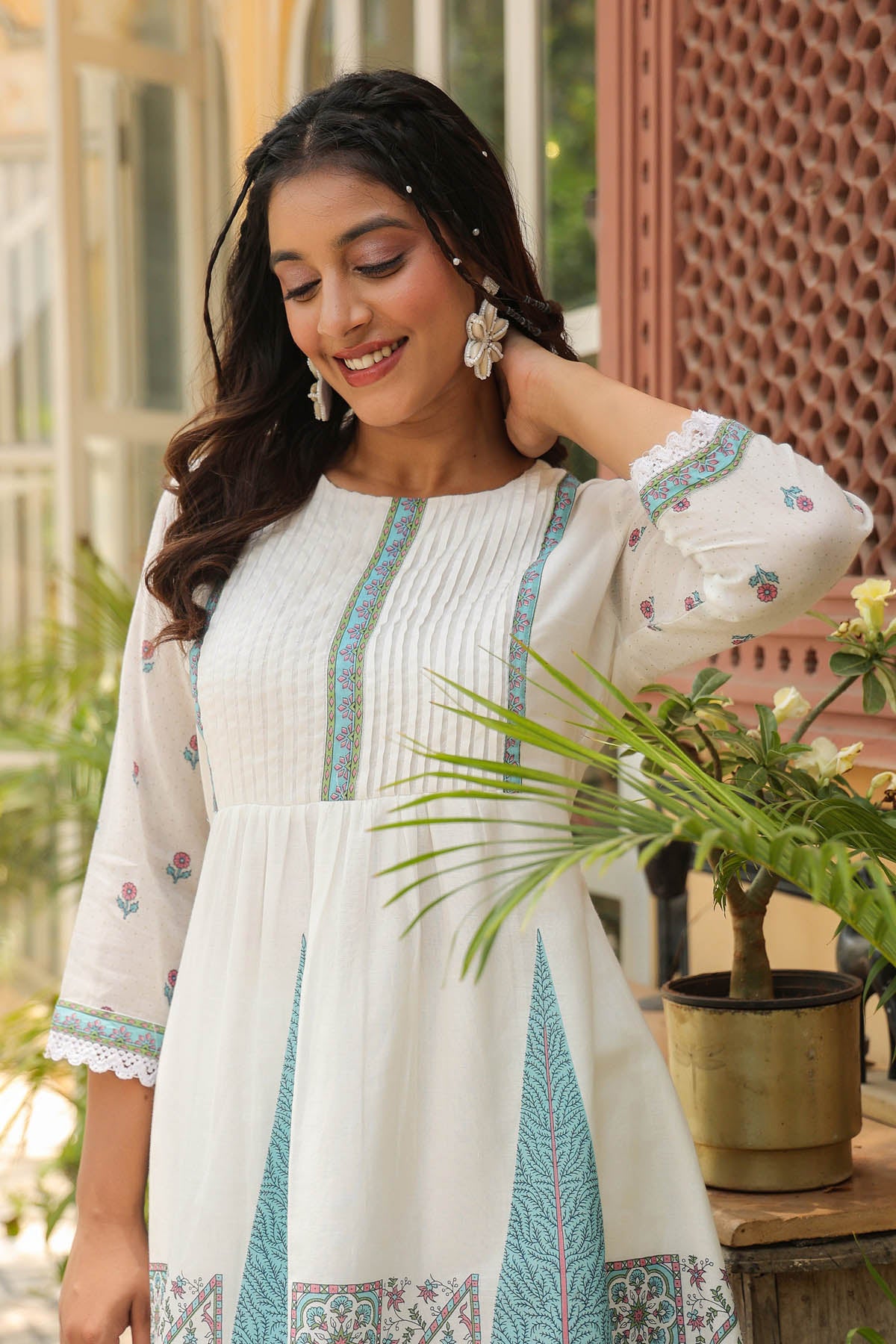 Woman wearing a white dress with blue embroidery in an outdoor setting