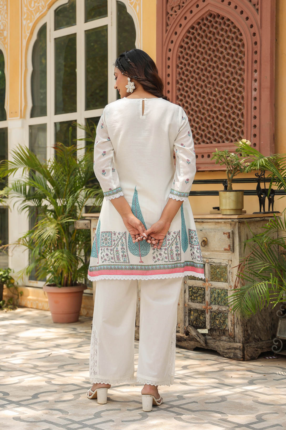 Woman in a traditional outfit standing in front of a decorative building entrance.