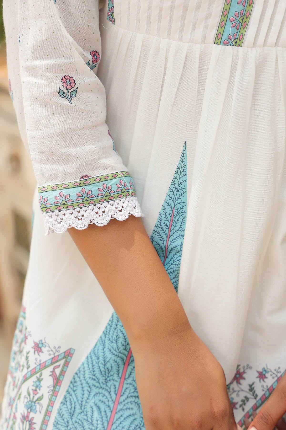 Close-up of a person wearing a white dress with floral embroidery and colorful patterns.