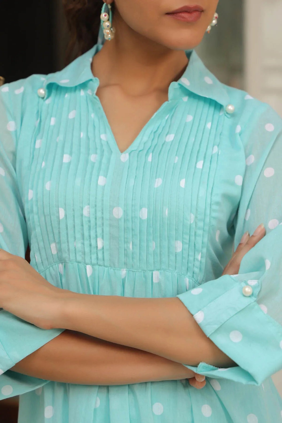 Person wearing a light blue dress with white polka dots and pearl buttons.