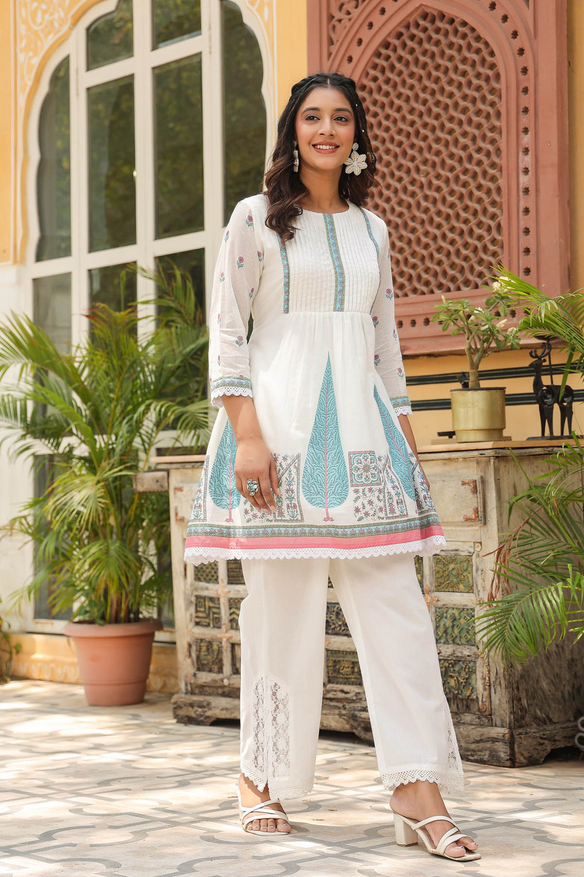 Woman in a traditional outfit standing in front of an ornate building with plants.