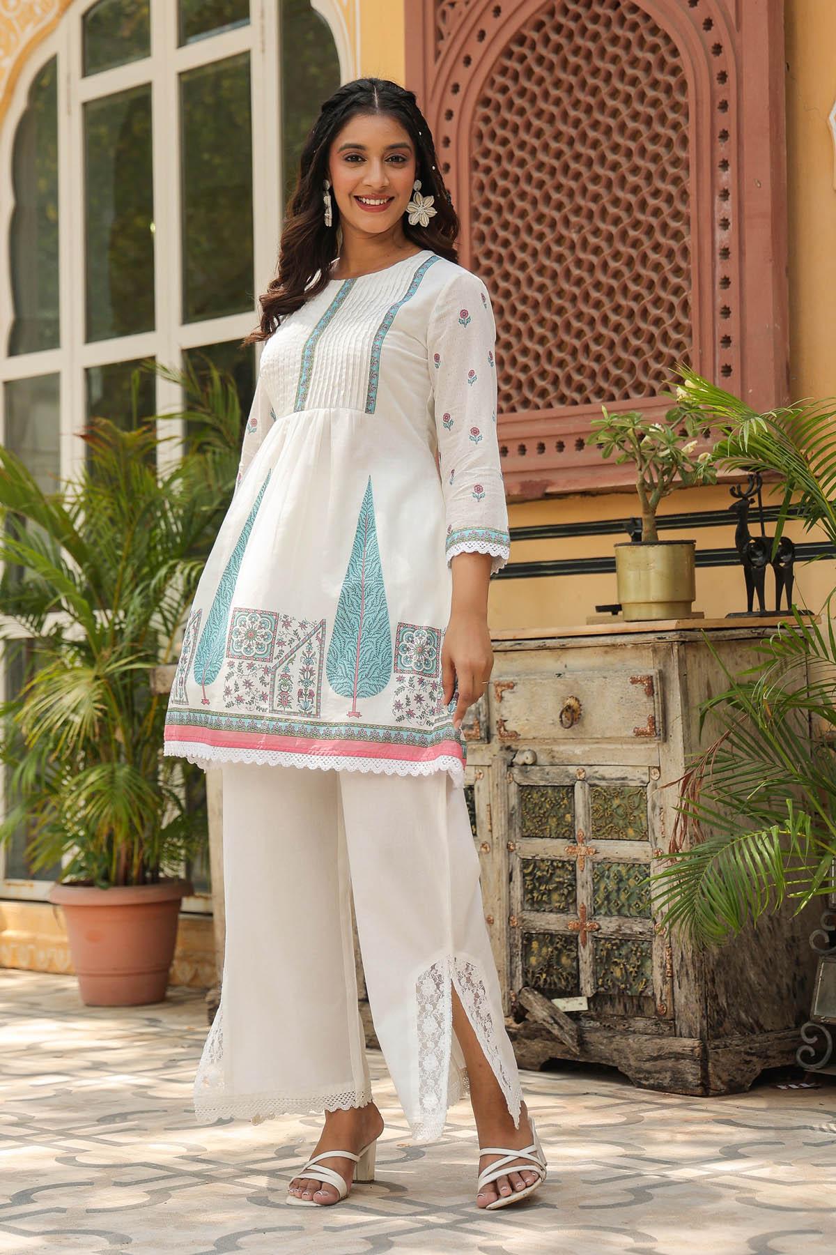 Woman in a white traditional outfit with blue embroidery standing in an outdoor setting.