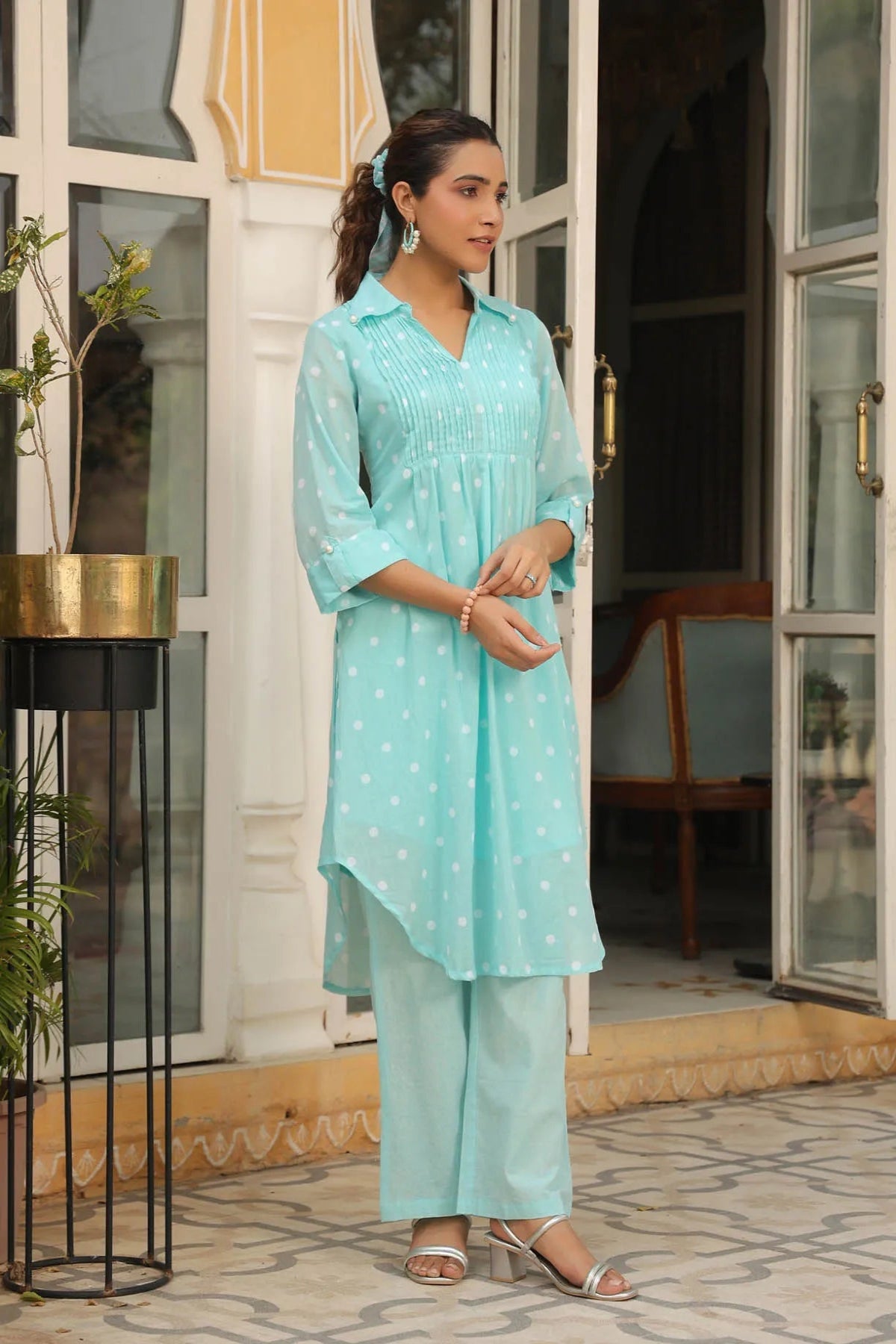 Woman wearing a light blue traditional outfit standing in front of a building entrance.
