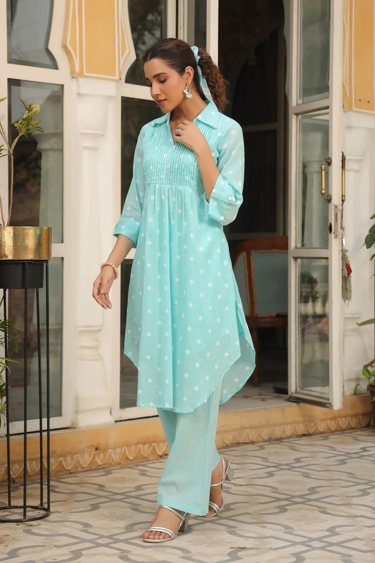 Woman wearing a light blue traditional outfit standing in front of a building entrance.