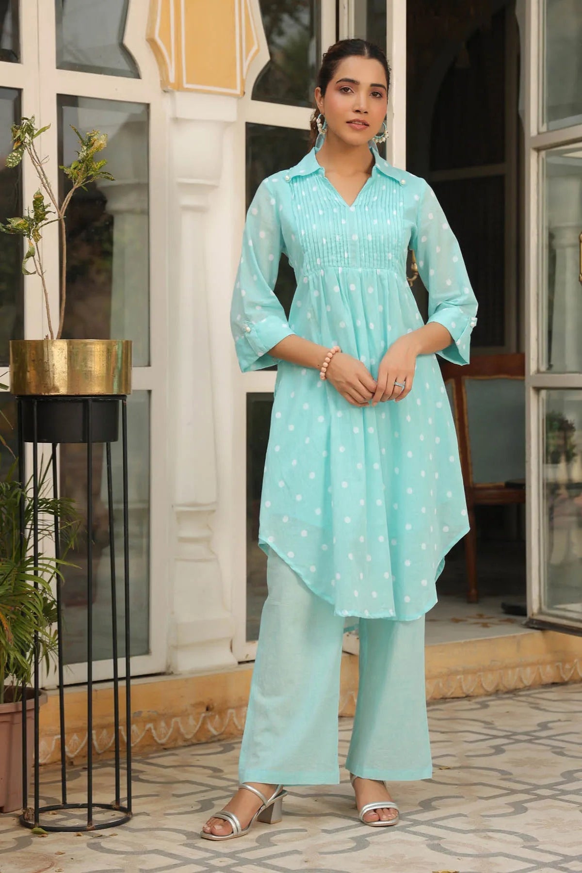 Woman wearing a light blue traditional outfit standing in front of a building entrance.