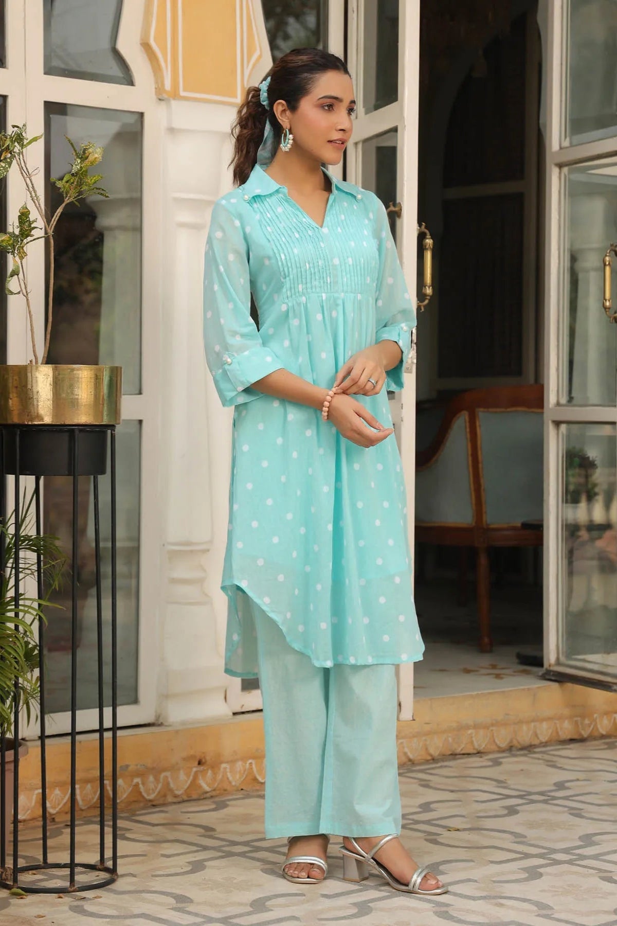 Woman in a light blue traditional outfit standing in front of a building entrance.