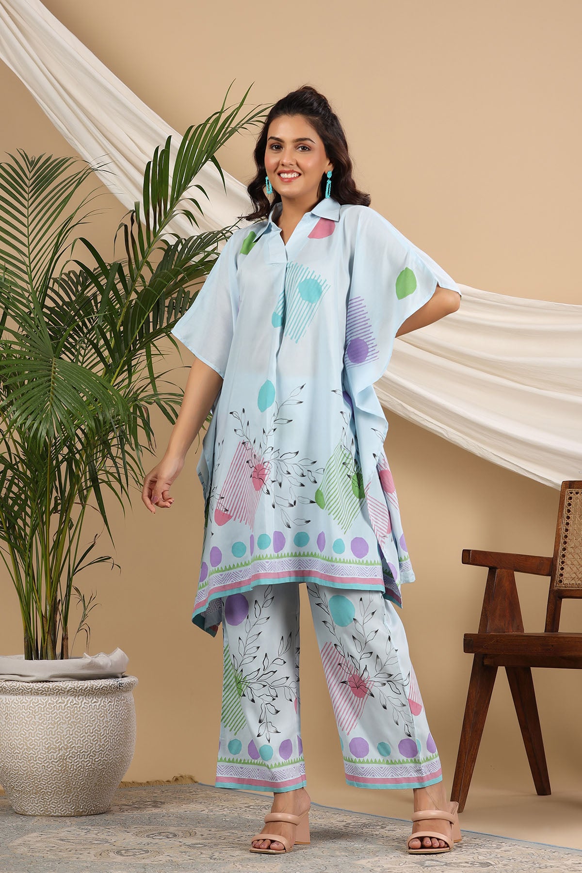 Woman wearing a light blue and multicolor outfit with a plant and chair in the background