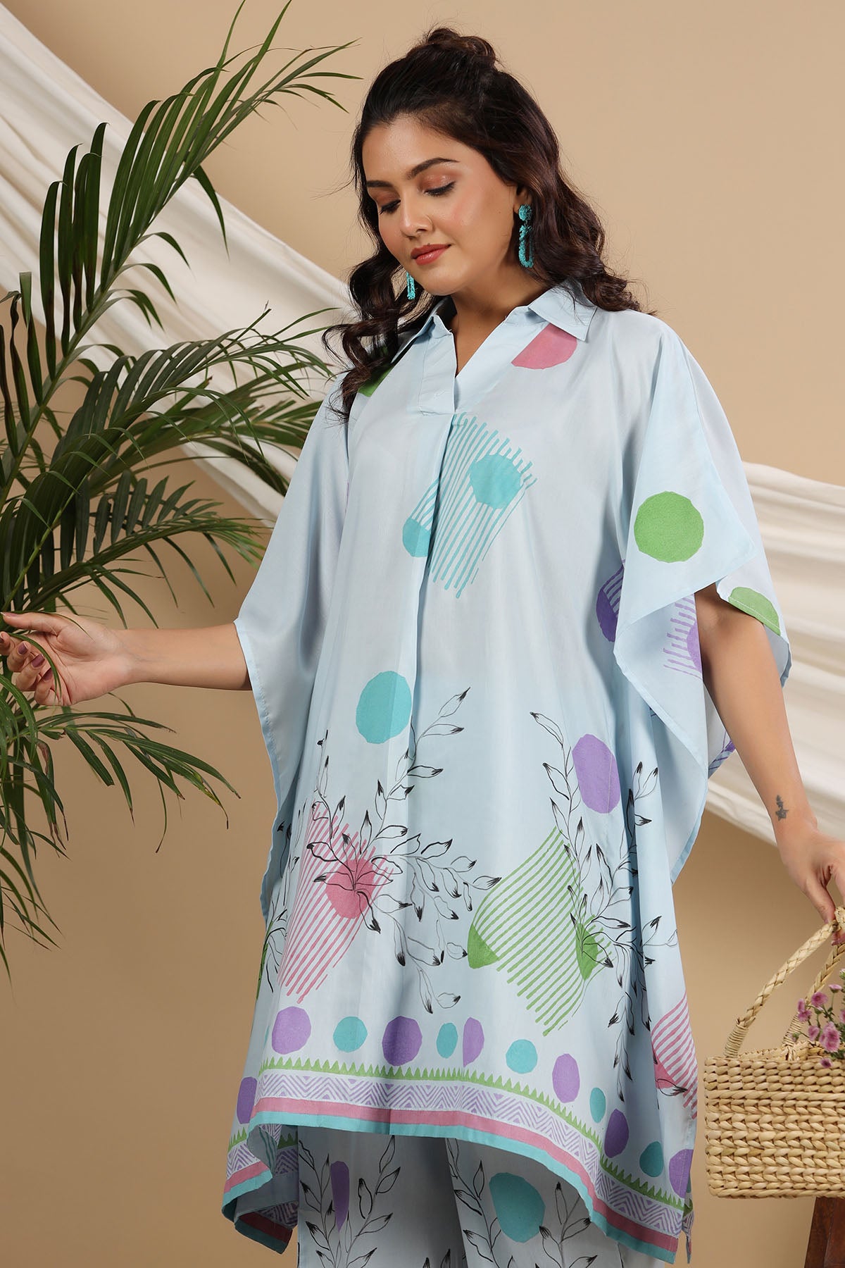 Woman wearing a light blue dress with colorful patterns, standing next to a plant.