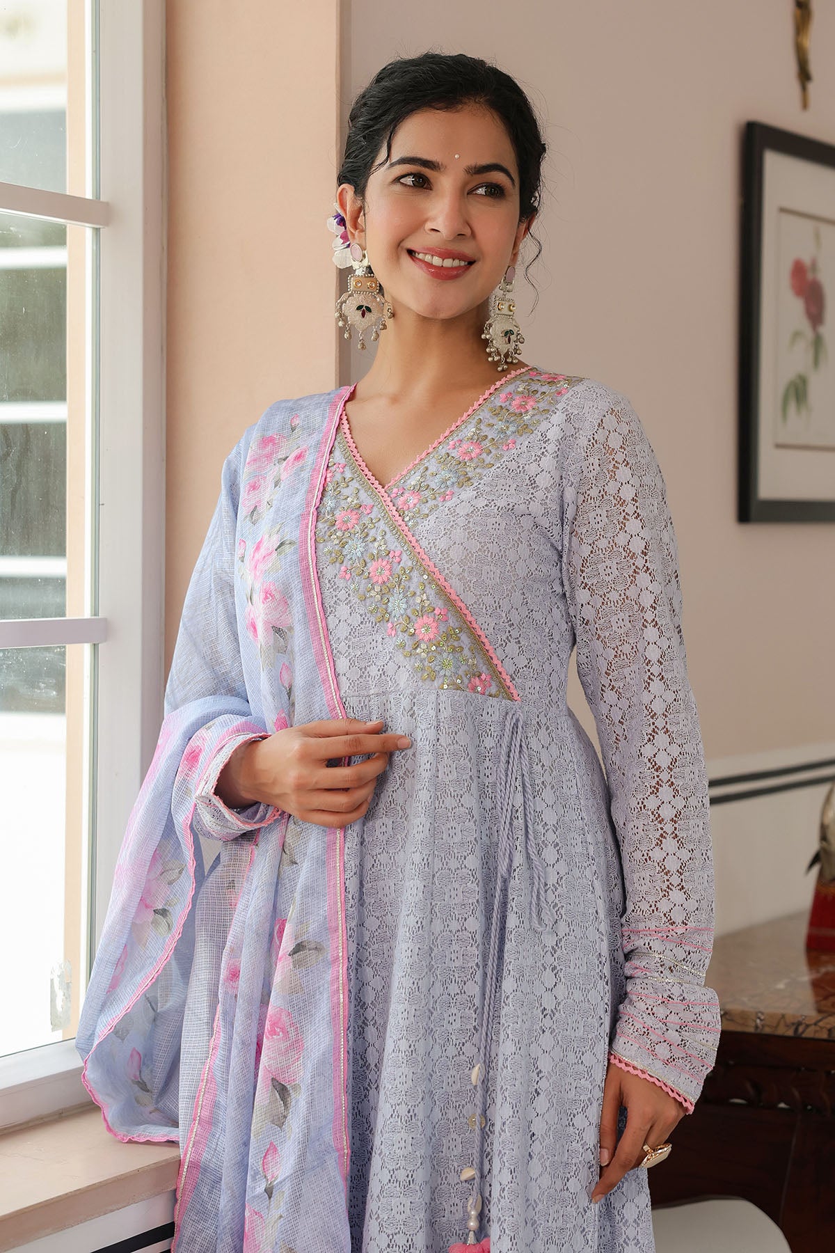 Woman wearing a light blue embroidered traditional outfit with pink accents indoors.