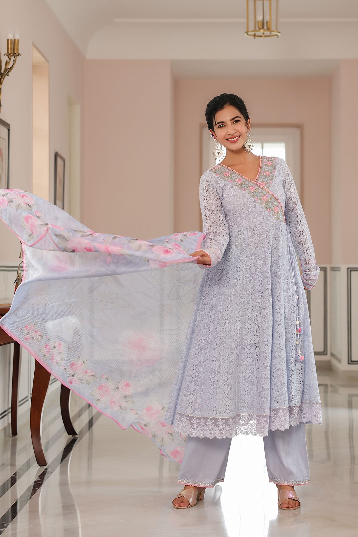 Woman in a light gray traditional outfit with floral patterns in a well-lit room.