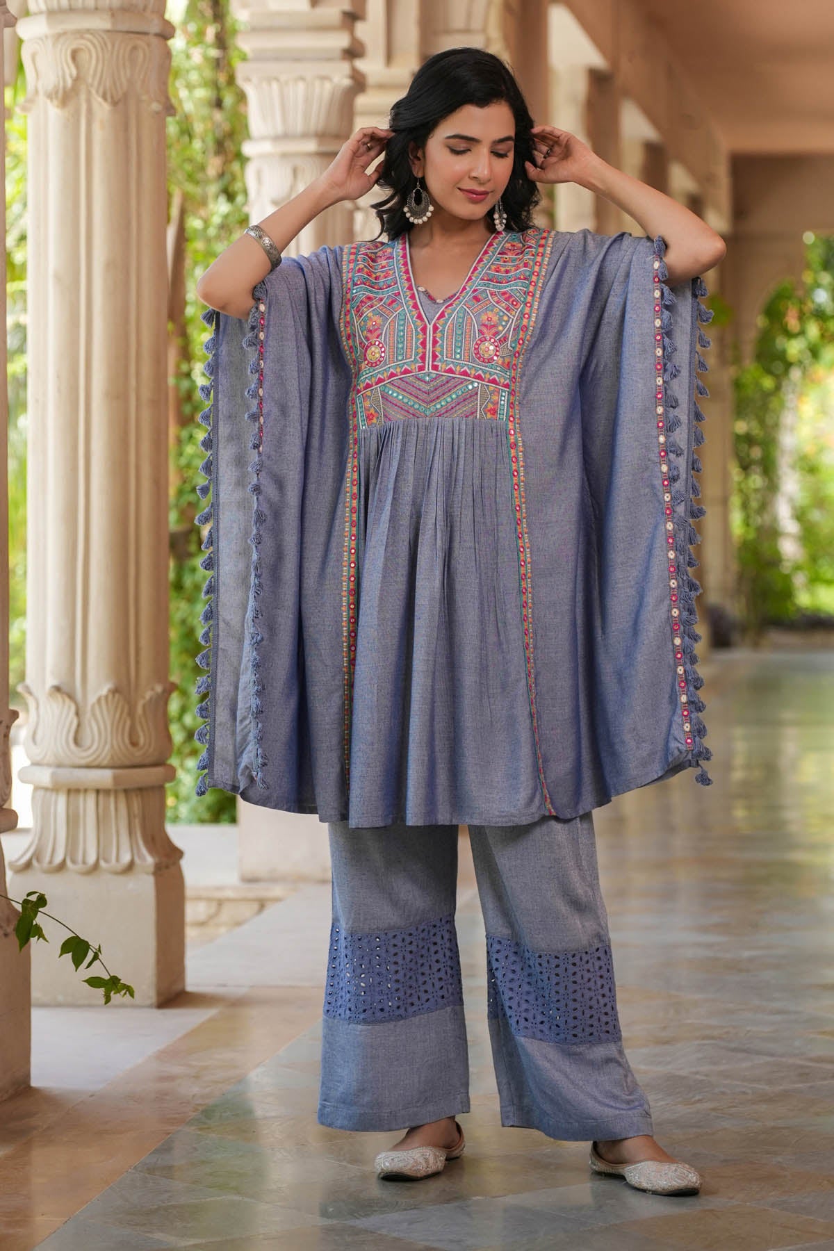 Woman wearing a traditional outfit with embroidered top and pants in an outdoor setting.