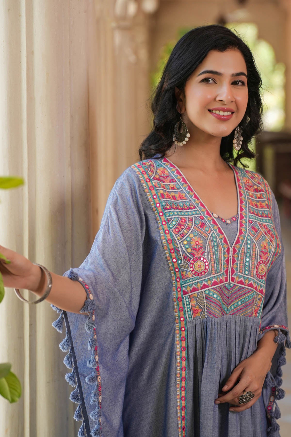 Woman wearing a blue embroidered dress with colorful patterns indoors.