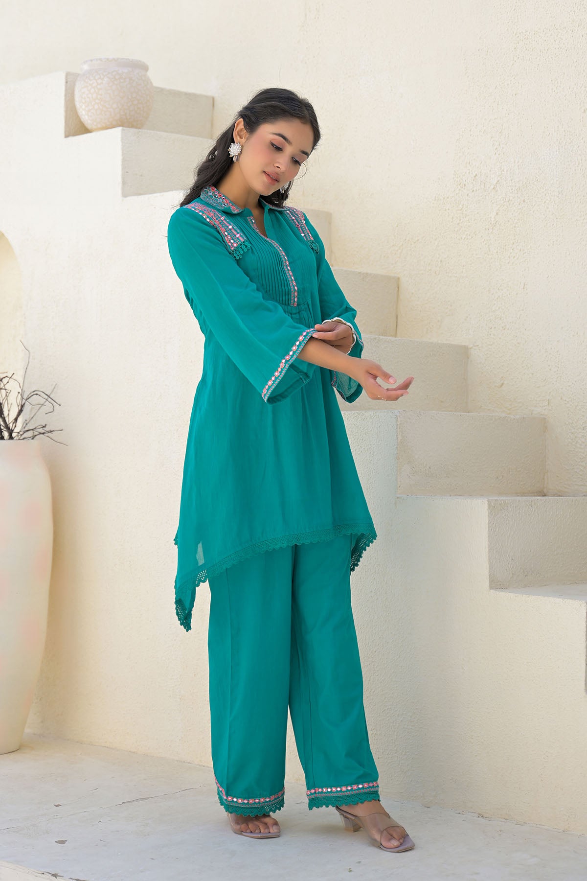 Woman wearing a teal traditional outfit with white embroidery in a minimalistic setting.