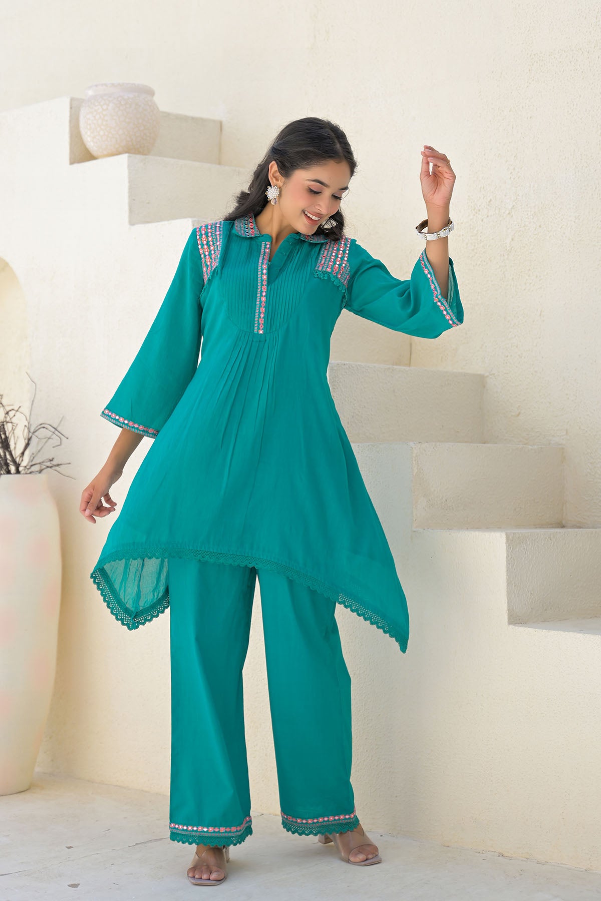 Woman wearing a teal traditional outfit with white embroidery in a minimalistic setting.