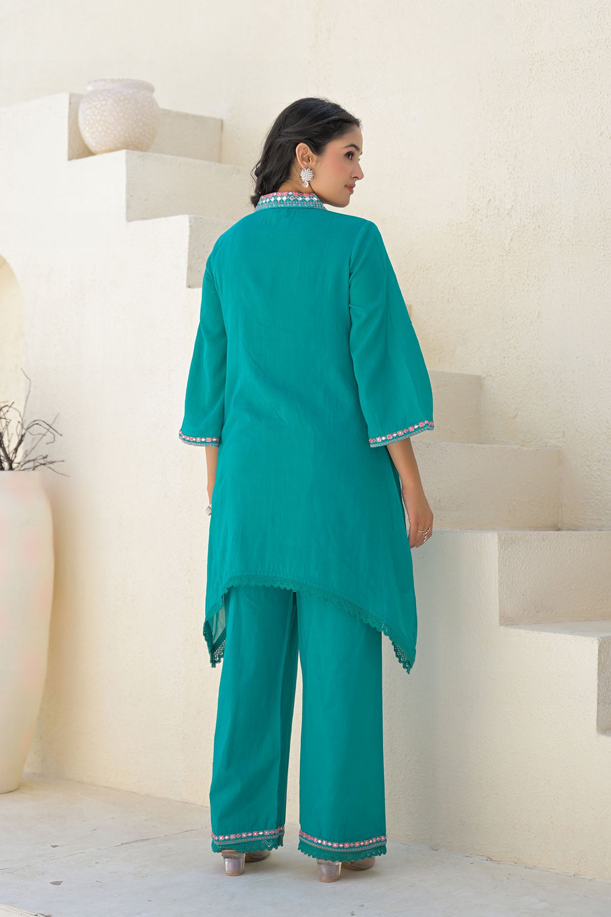 Woman wearing a teal traditional outfit with white embroidery in a minimalistic setting.