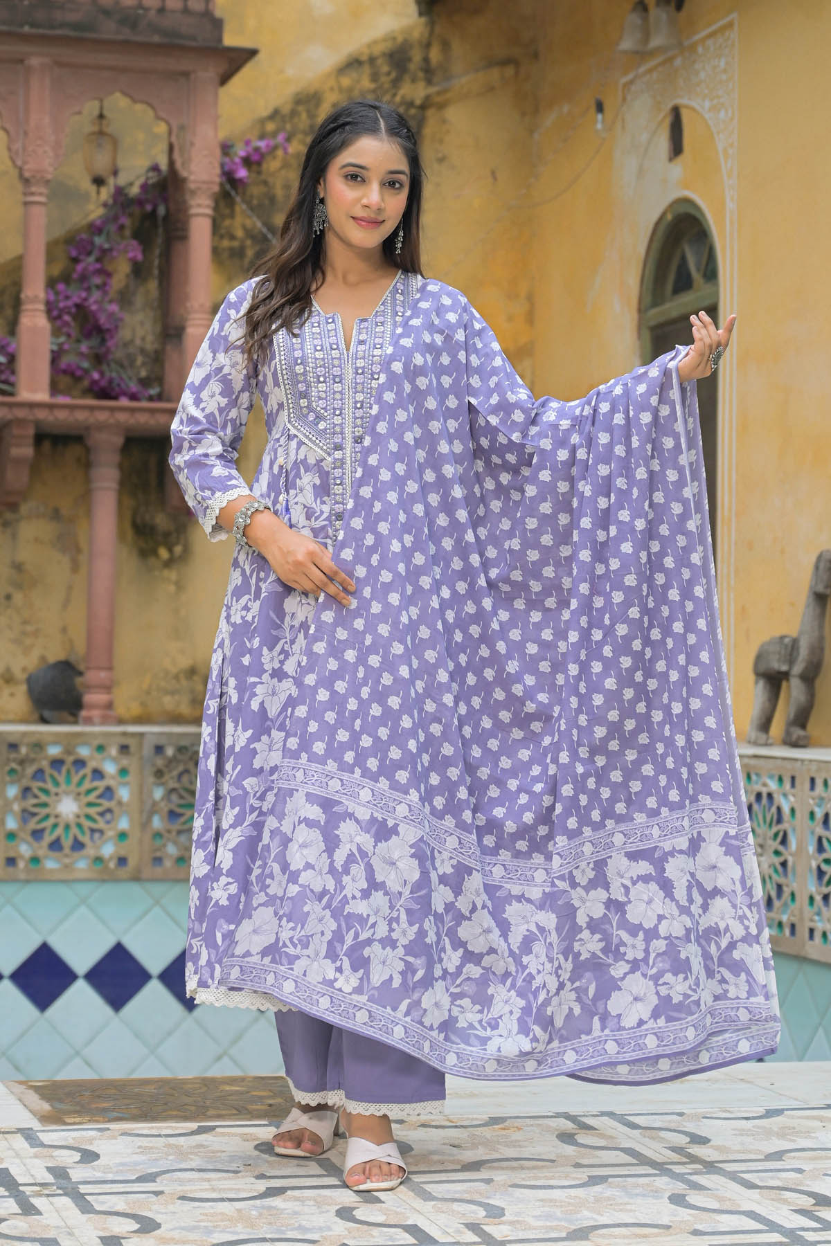 Woman in a purple floral dress standing in front of a decorative wall.
