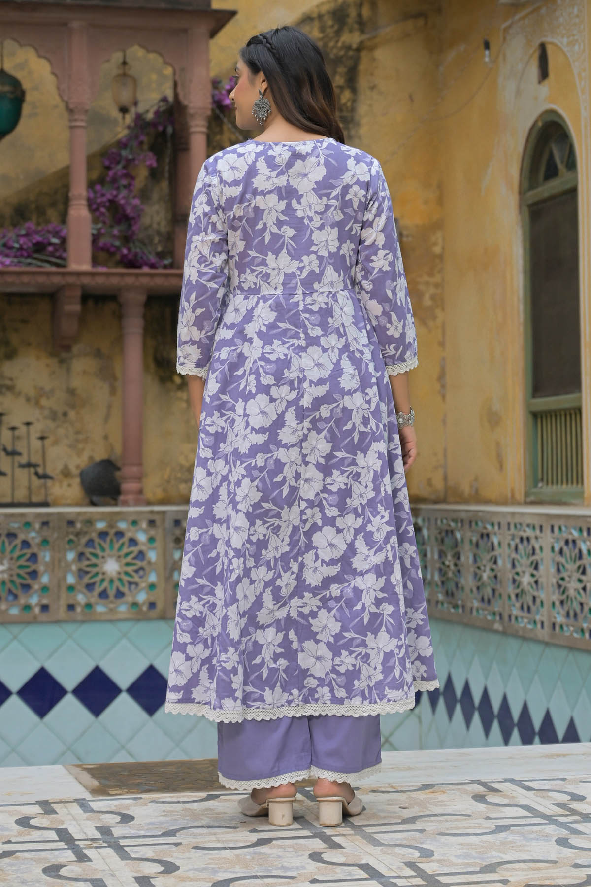 Woman wearing a purple floral kurta with white pants standing in front of a decorative building.