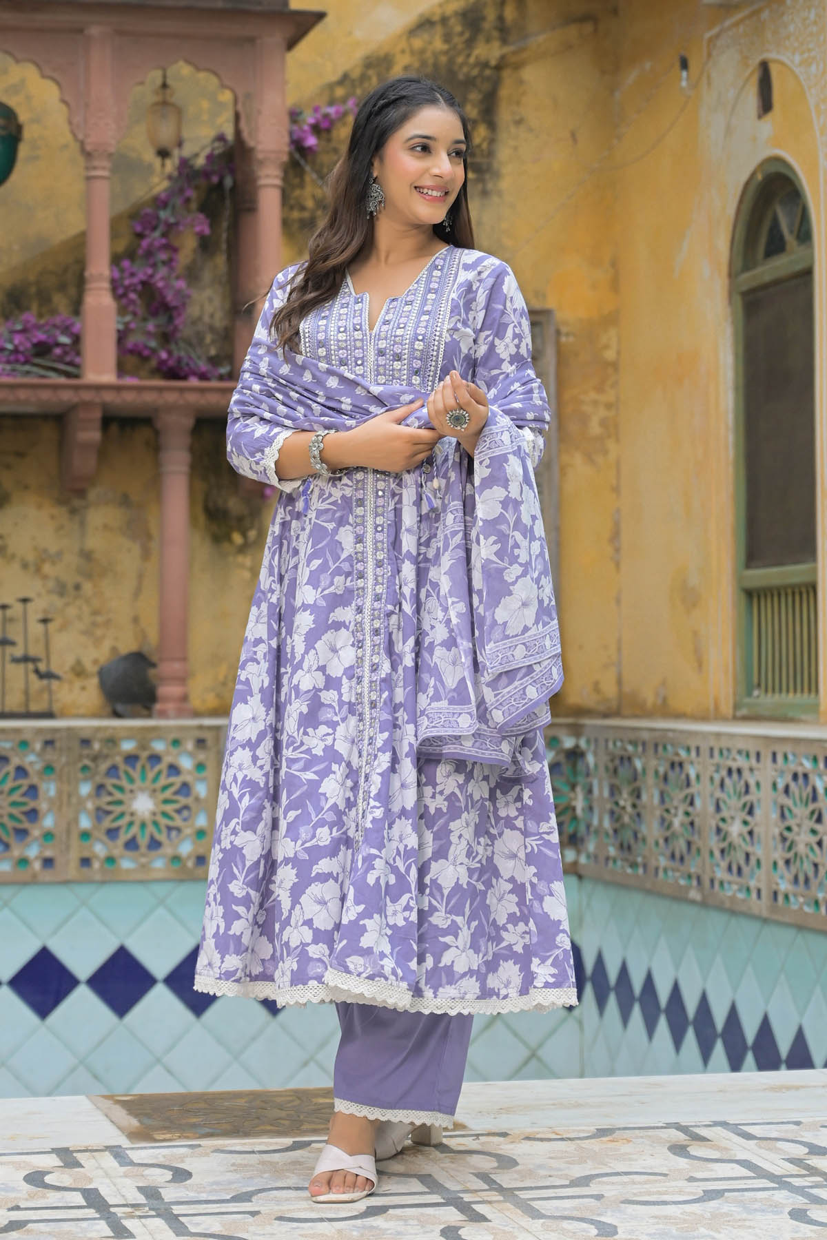 Woman in a purple floral outfit standing in front of a colorful architectural background