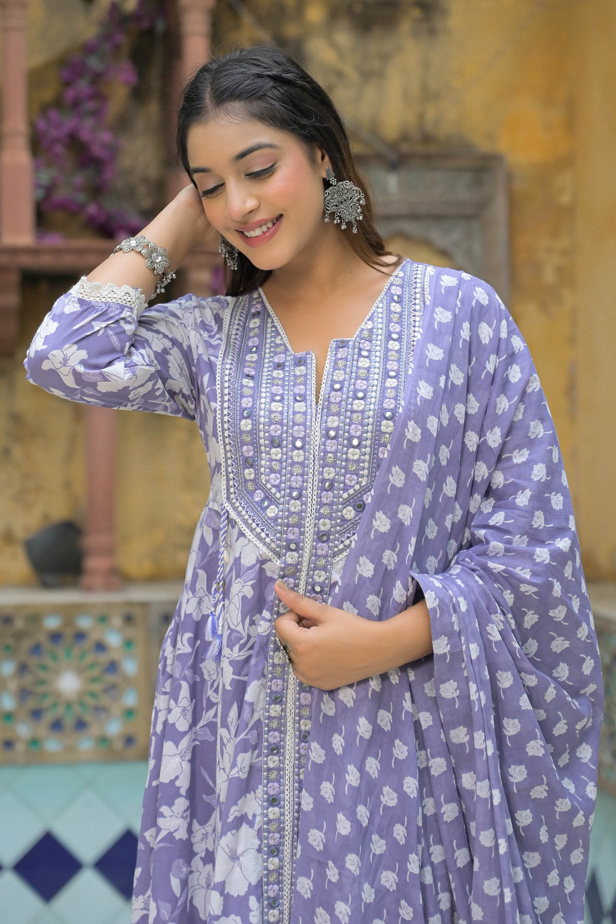 Woman wearing a purple traditional outfit with white patterns in an indoor setting.