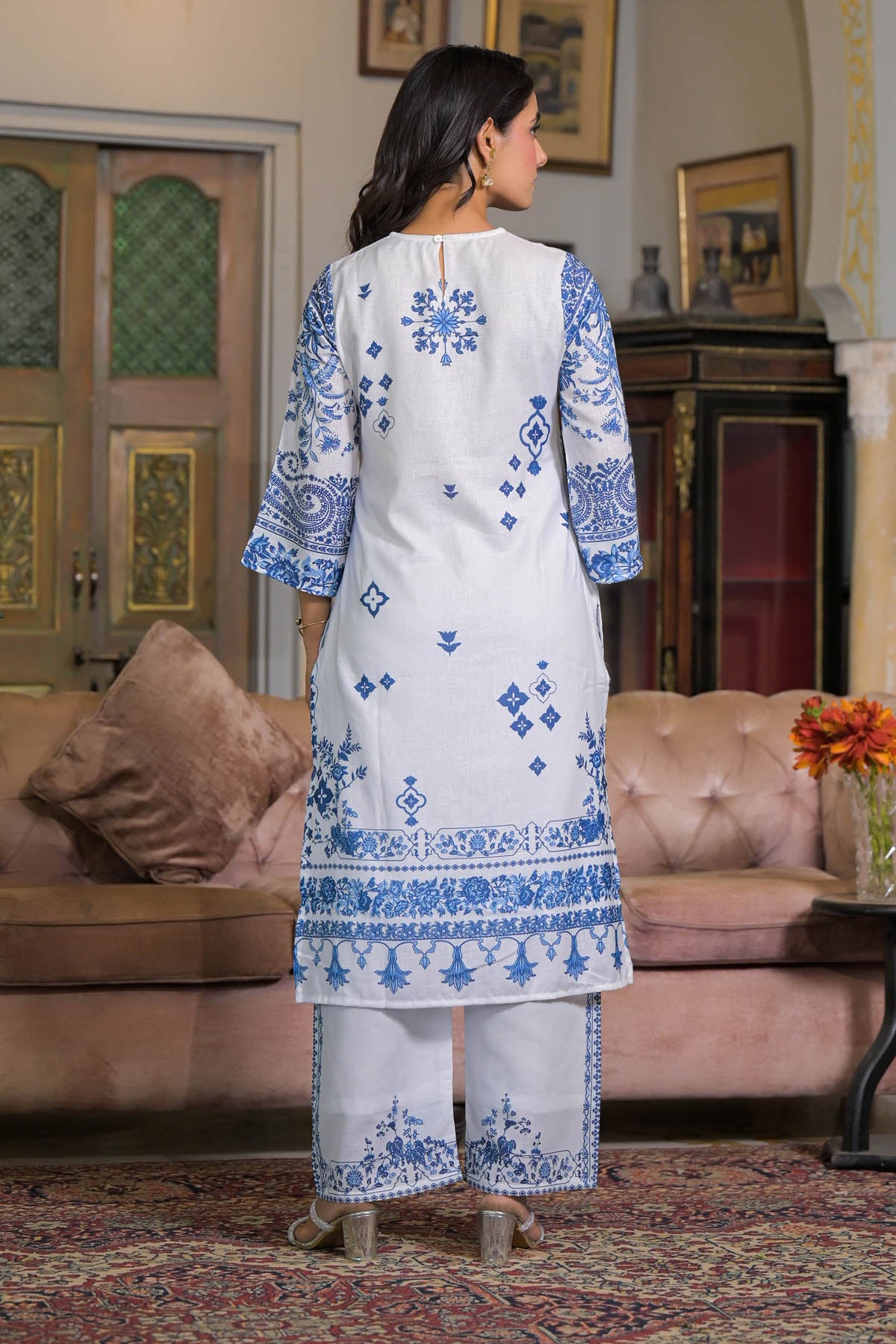 Woman in a white and blue embroidered traditional outfit standing in a living room.