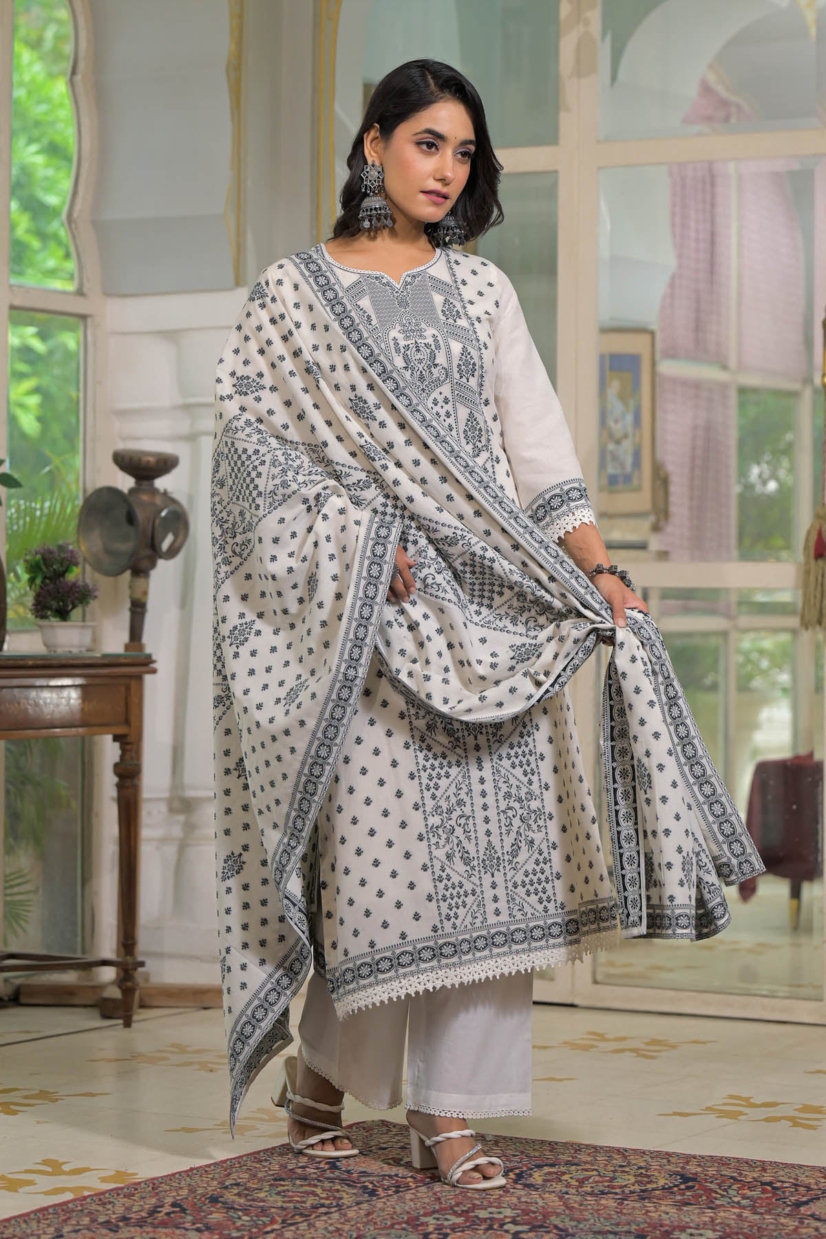 Woman wearing a traditional outfit with a white and black patterned dupatta in an elegant room.
