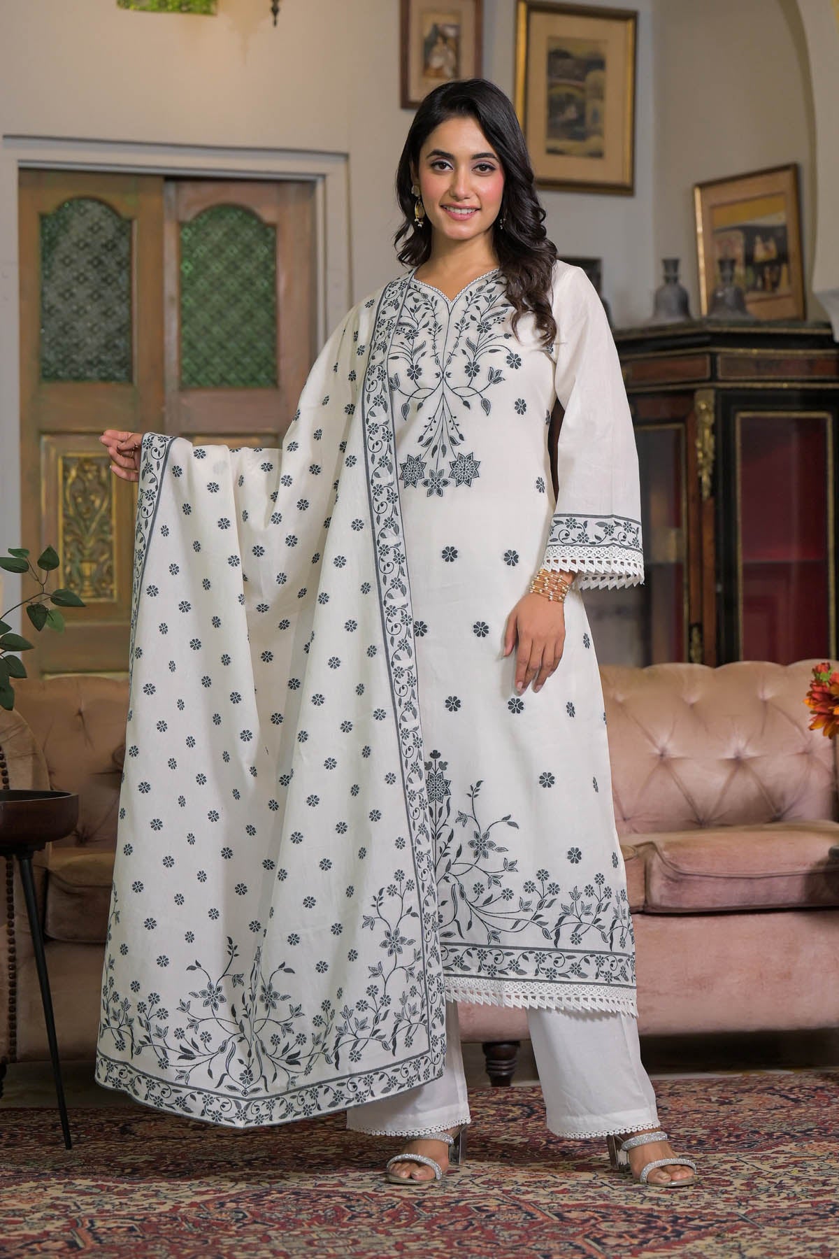 Woman in a white embroidered traditional outfit standing in a decorated room.