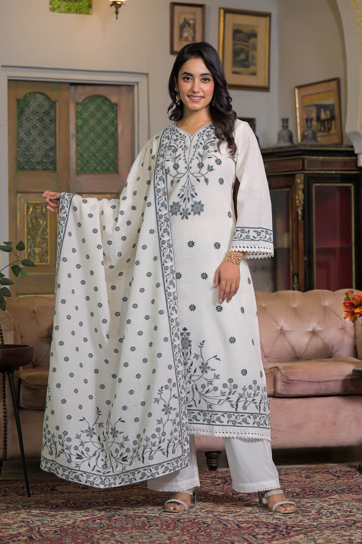 Woman in a white traditional outfit with embroidery in a decorated room.