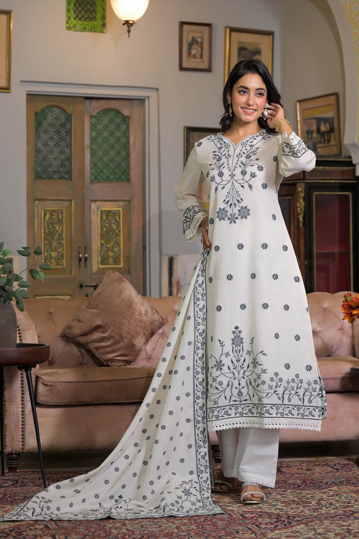 Woman in a white embroidered outfit standing in a living room.