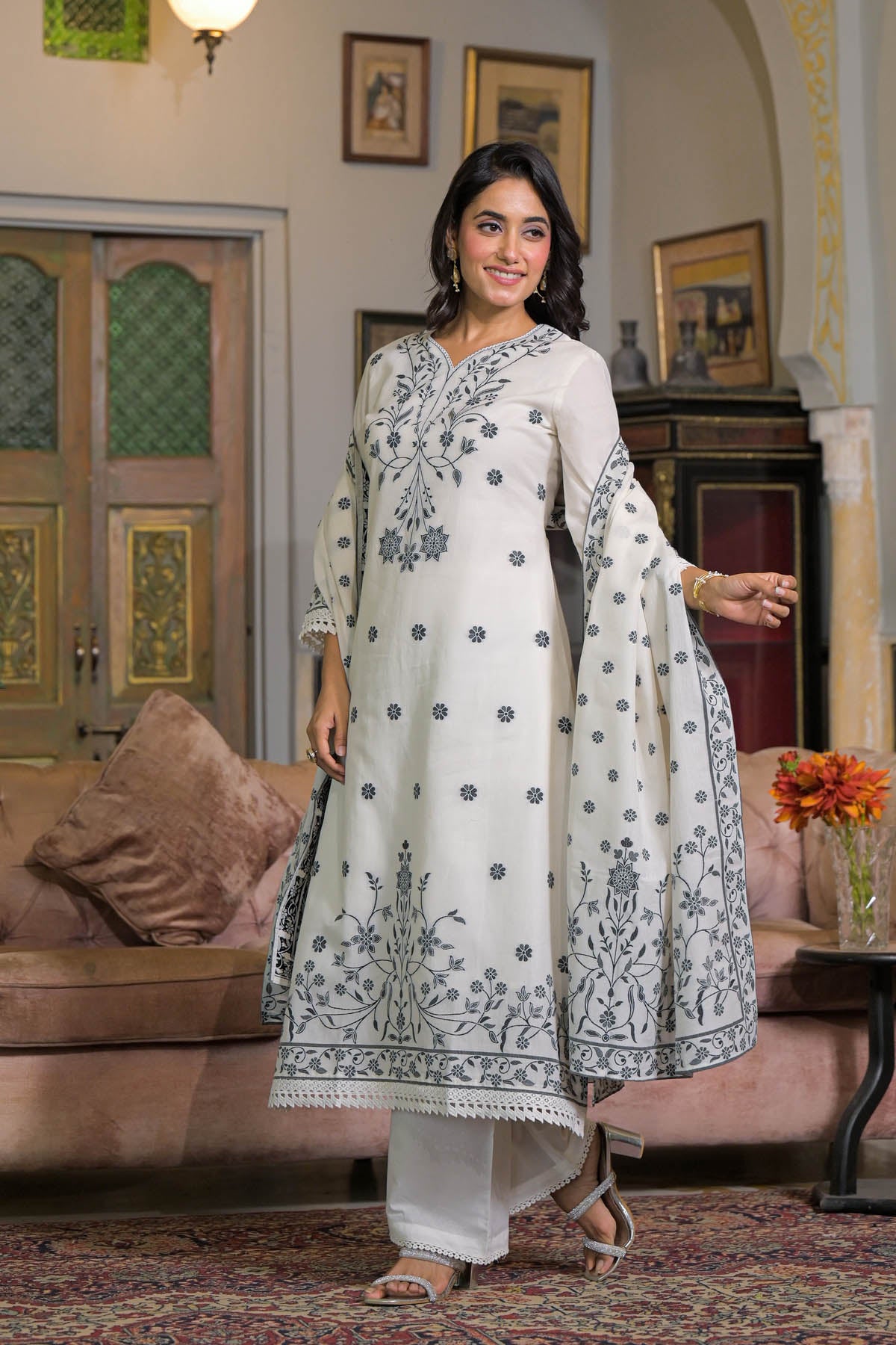 Woman in a white embroidered traditional outfit standing in a decorated room.