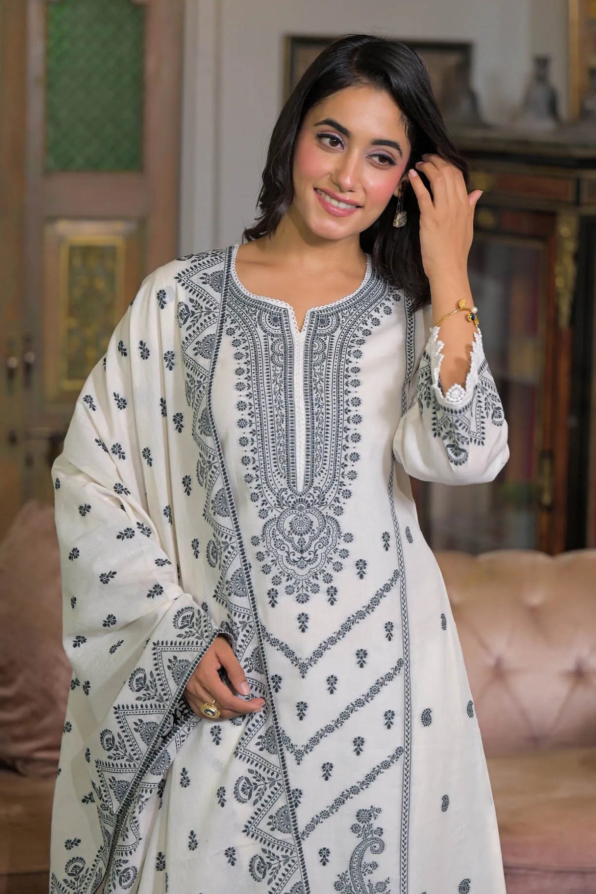 Woman wearing a white and black embroidered traditional outfit indoors.
