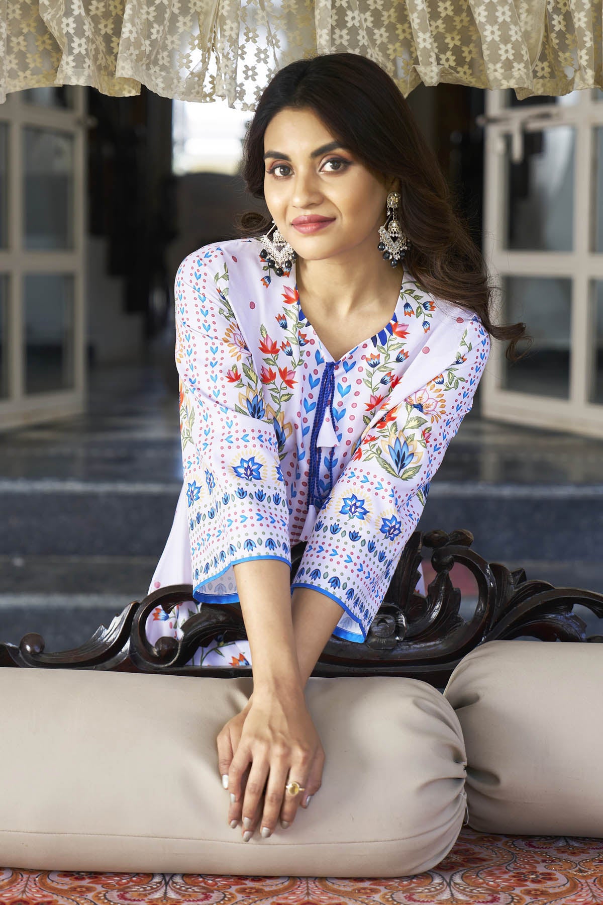Woman in a colorful embroidered outfit sitting on a decorative chair.