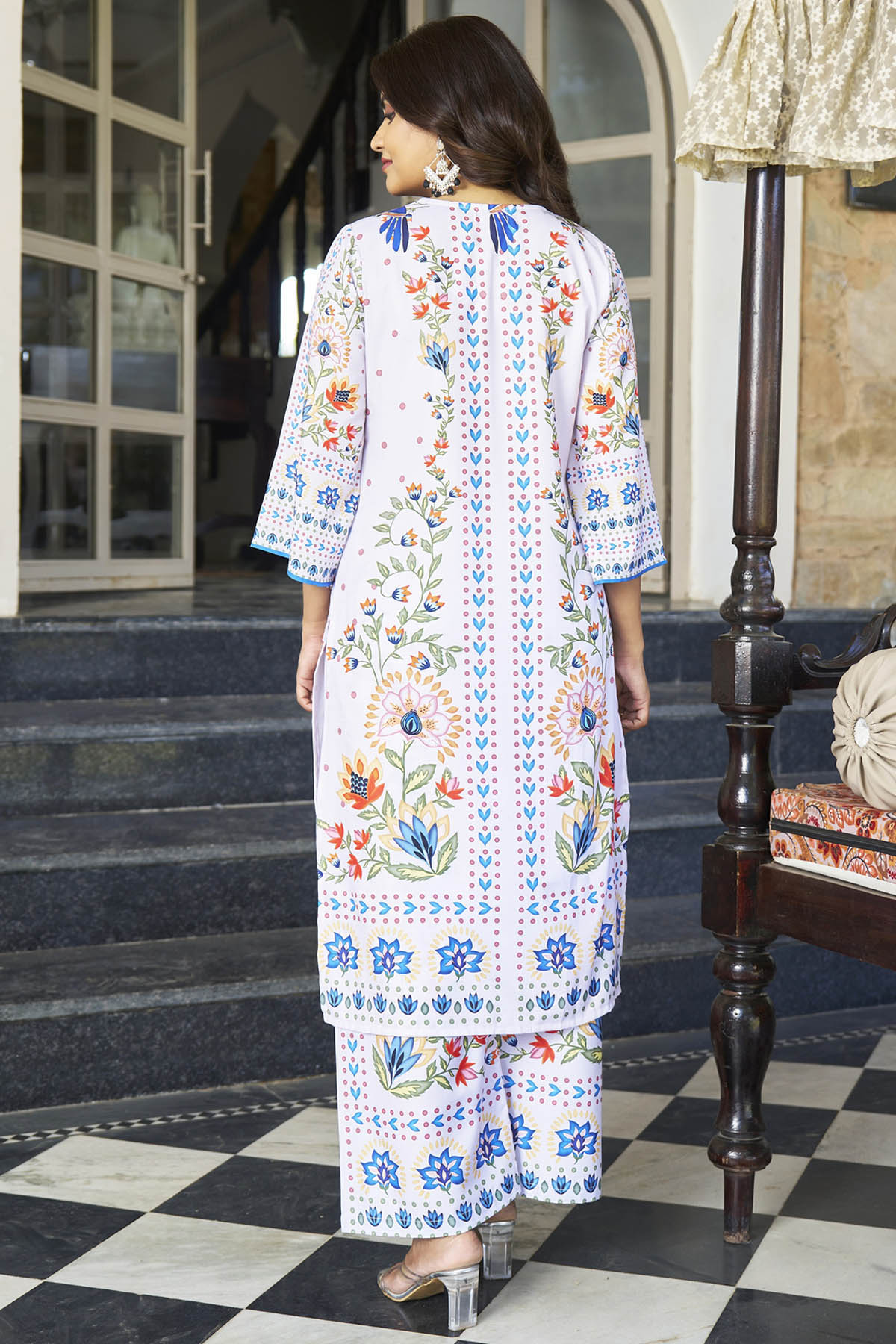 Woman wearing a colorful embroidered outfit standing in front of a building entrance.