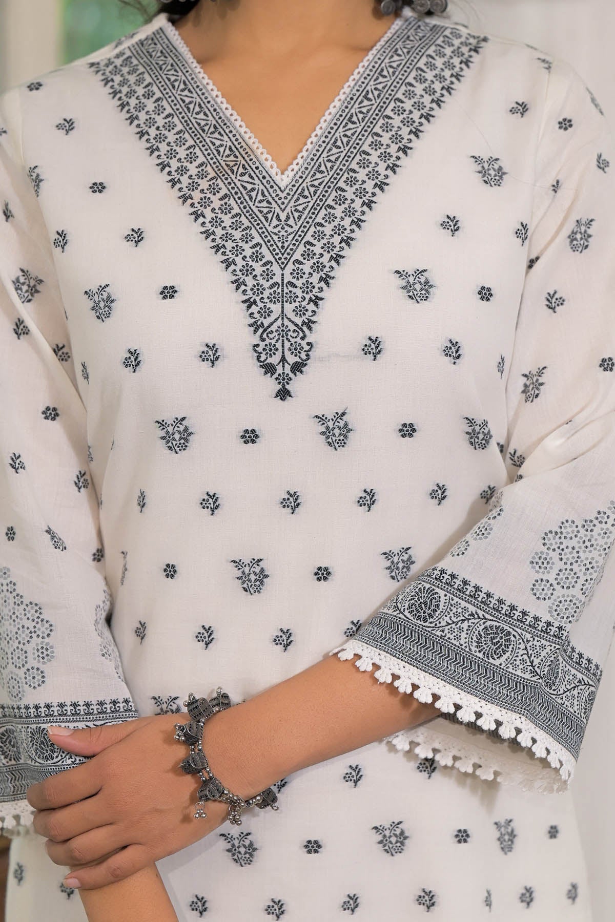White traditional outfit with black floral embroidery and pom-pom details.